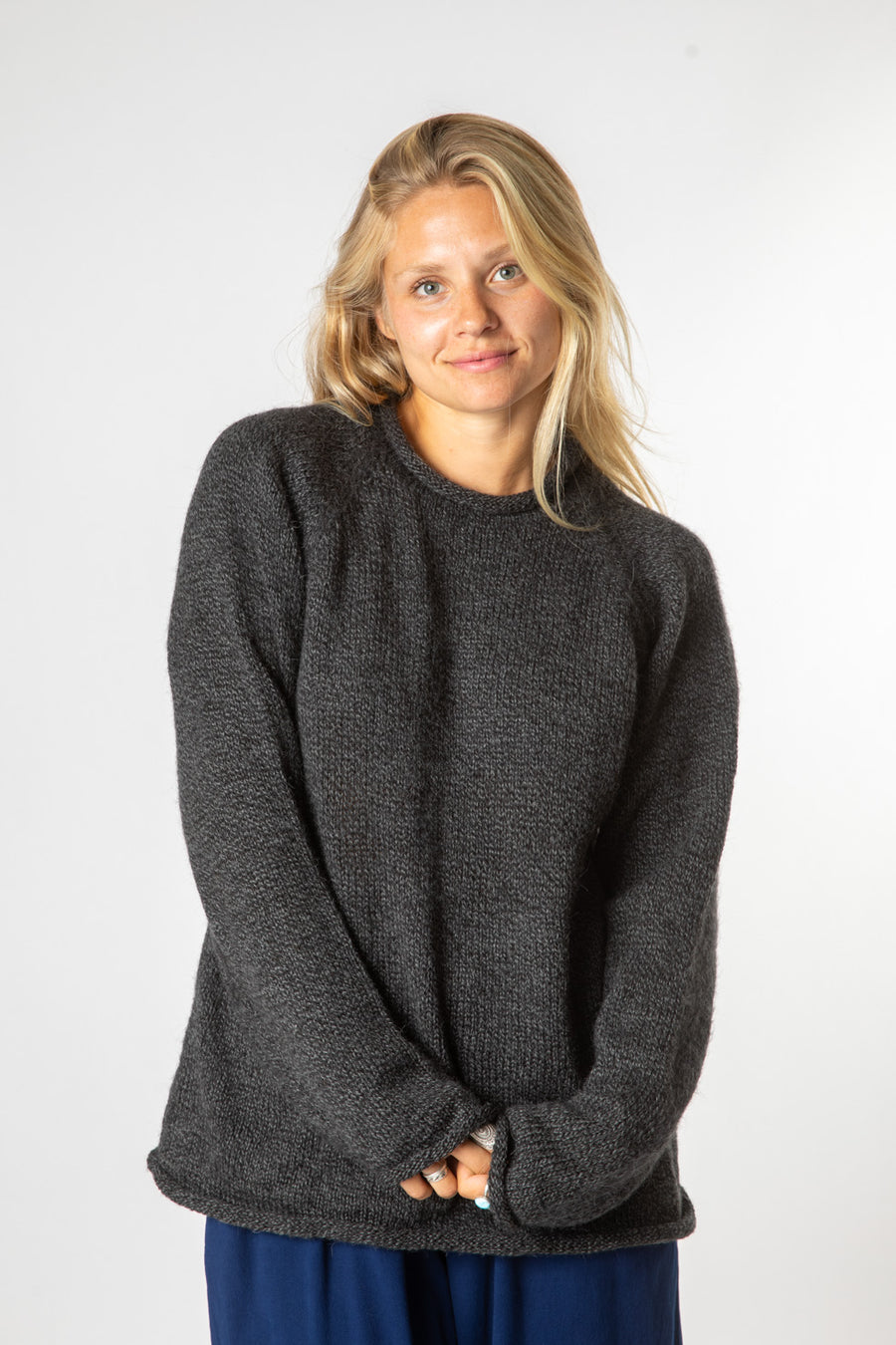 Beautiful blonde hippie woman wearing a charcoal colored alpaca sweater for women with blue trousers. 