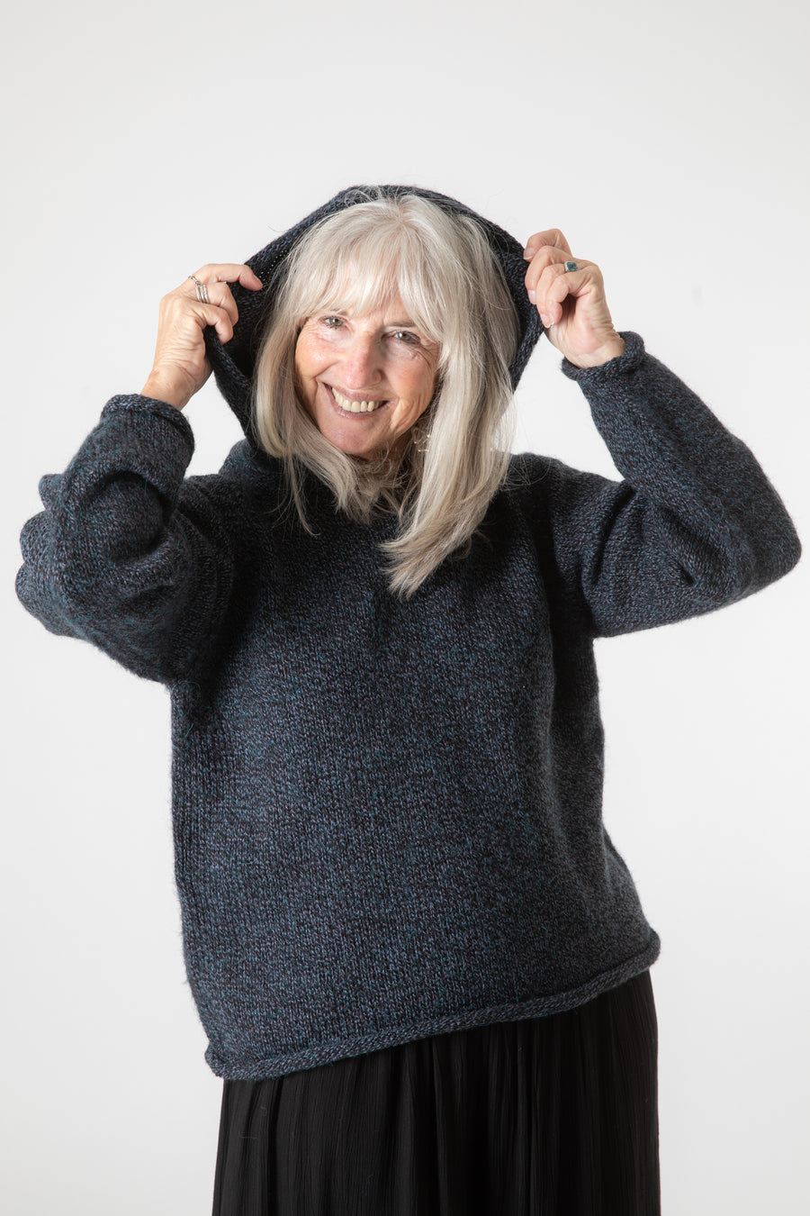 Beautiful white haired woman pulling up the hood of a dark blue alpaca hoodie sweater with a black hippie skirt. 