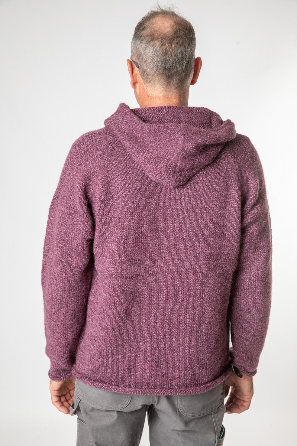 Hippie man facing backwards wearing a plum colored alpaca sweater for men with a hood and gray hippie pants. 