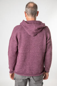 Hippie man facing backwards wearing a plum colored alpaca sweater for men with a hood and gray hippie pants. 