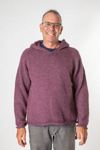 Happy hippie man with glasses smiling and wearing a plum colored alpaca hoodie and gray boho trousers. 