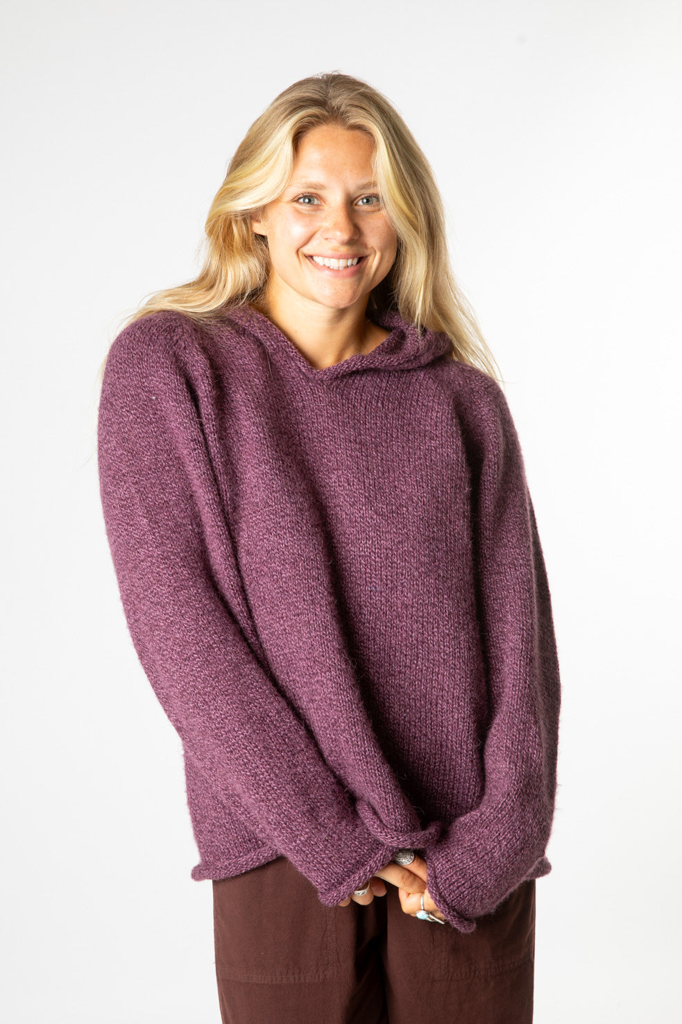 Happy blonde hippie girl wearing a purple alpaca hoodie sweater and brown hippie bottoms. 