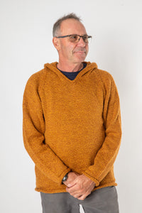 Hippie man with gray hair and glasses modeling a burnt orange alpaca hoodie and gray khaki pants. 