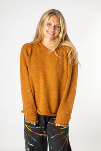 Beautiful blonde hippie girl smiling and wearing a sunflower colored alpaca sweater for women and back tie dye bottoms. 