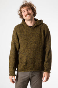 Happy bohemian man with curly brown hair and a mustache smiling and wearing a yellow and black hand kitted alpaca hoodie with tan hippie trousers. 