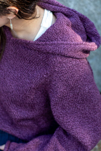 Detailed photo of a brunette woman with silver feather earrings wearing a hooded women's alpaca sweater in plum