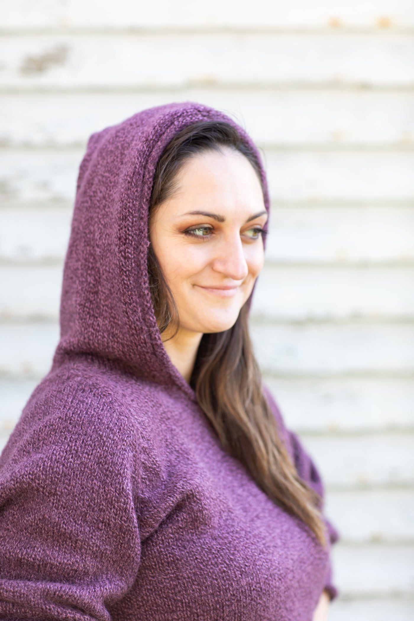 Detail photo of a beautiful brunette hippie woman with brown eyes wearing a plum colord women's alpaca hoodie and staring into the distance