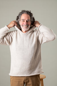 Happy bohemian man with gray hair and a white beard pulling up the hood of his white alpaca hoodie wearing tan hippie trousers. 