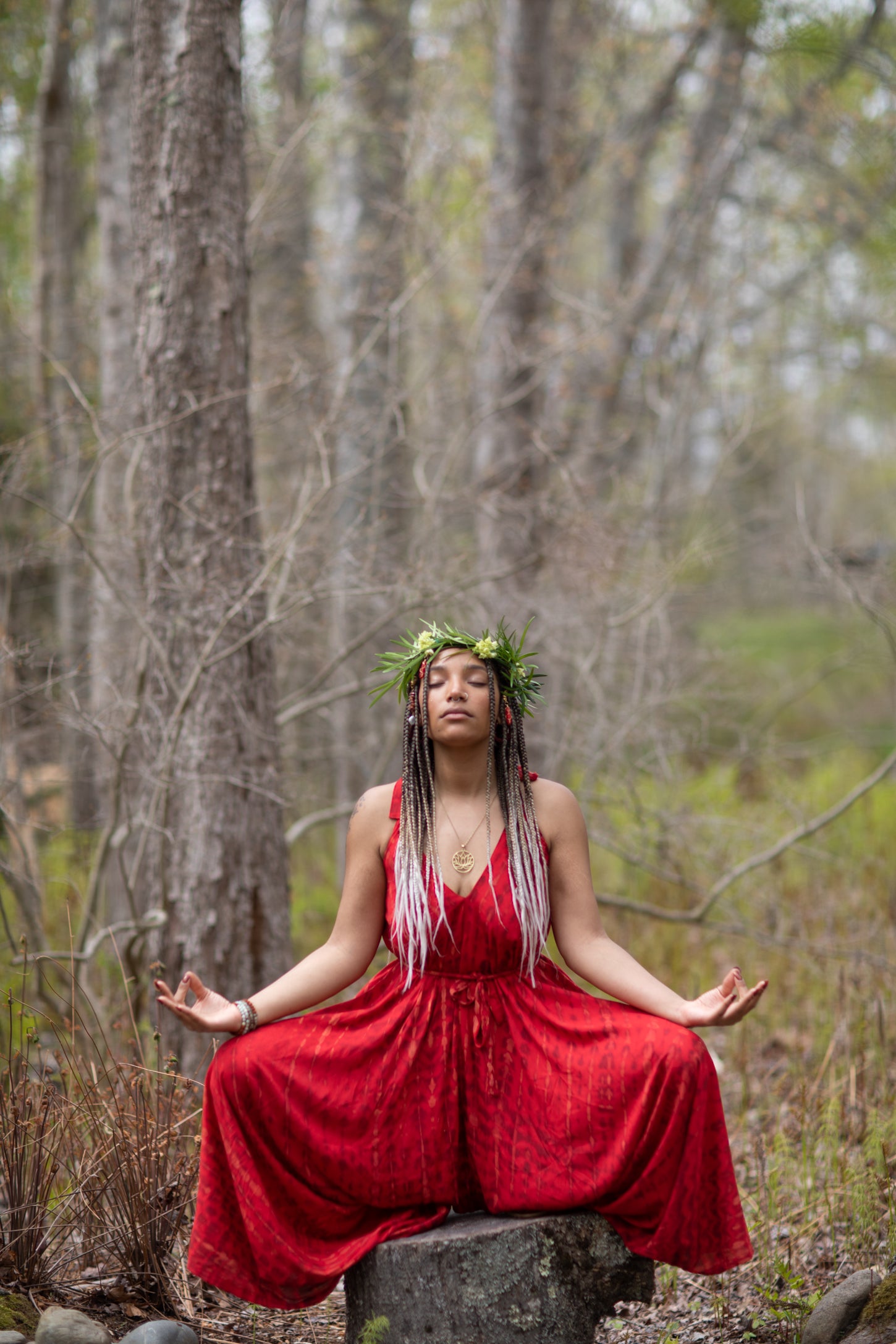 beautiful hippie woman wearing a flower crown doing a salutation yoga pose in a red flowy one piece dress in the forest